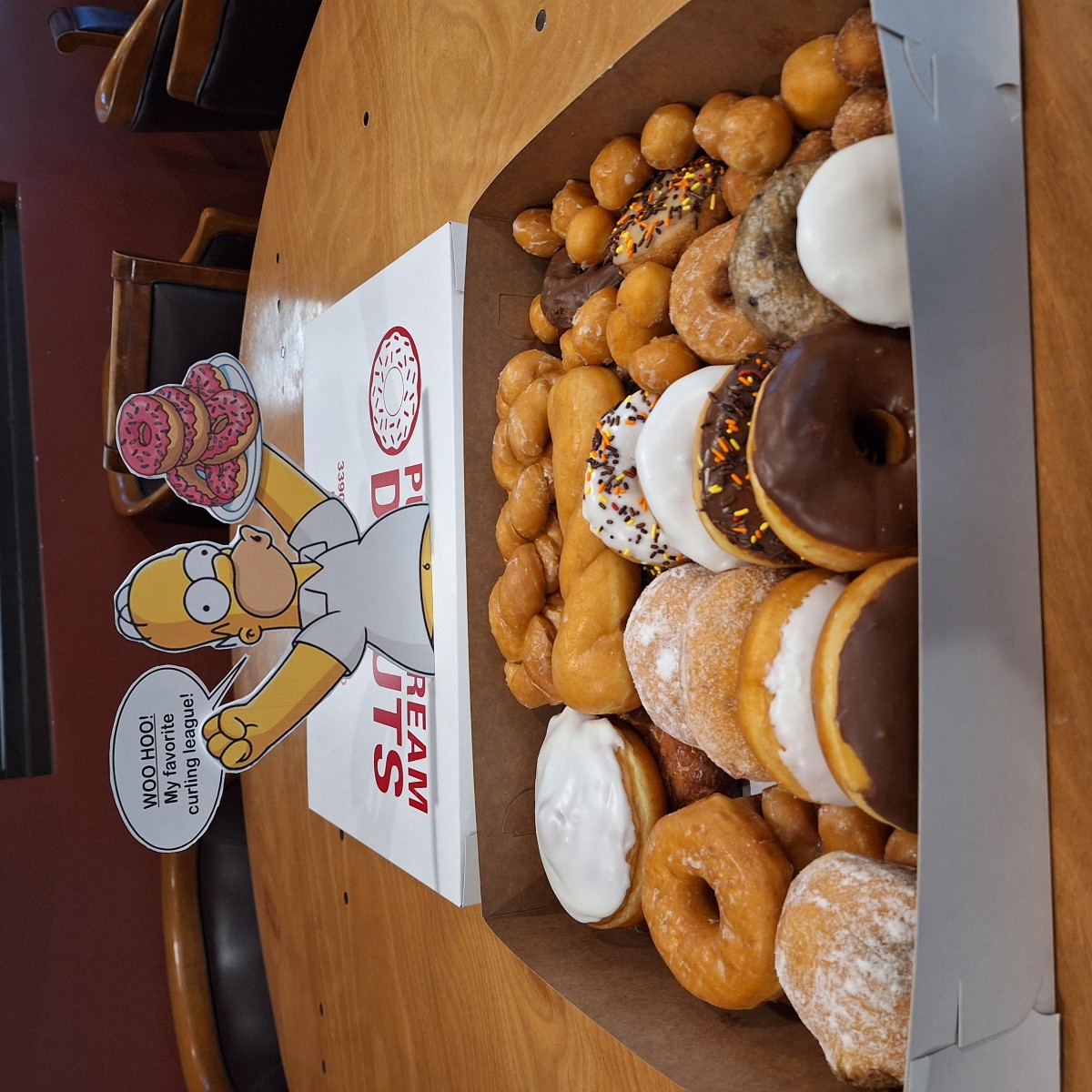 A box of donuts in the club room with a Homer Simpson cutout saying woo hoo, my favorite curling league